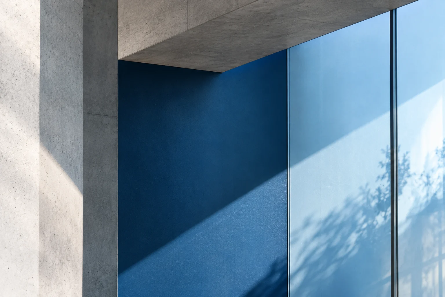 A peacock blue wall and glass panels framed by concrete in afternoon light